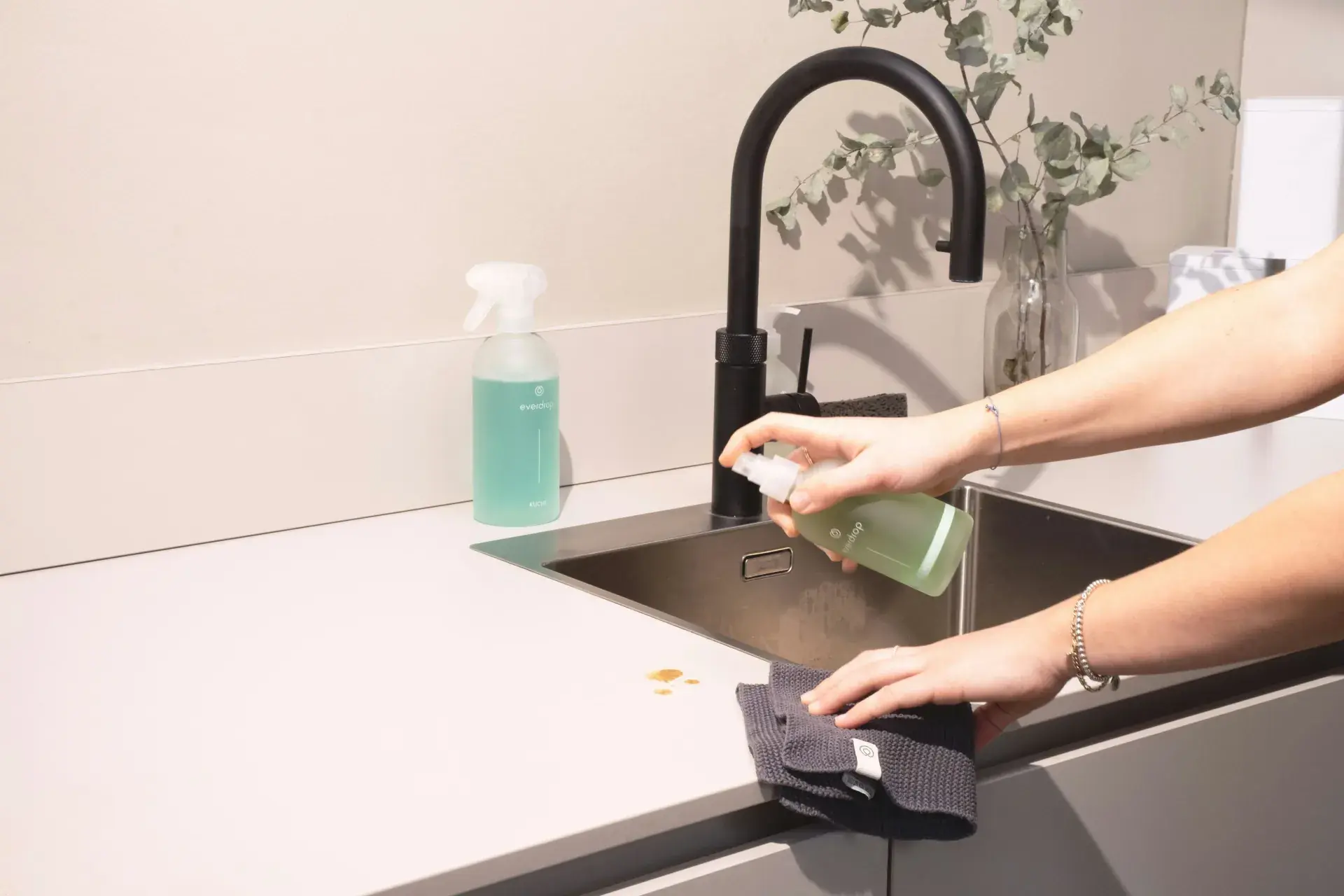 Städare sprayar rengöringsmedel och torkar av en diskbänk i ett kök